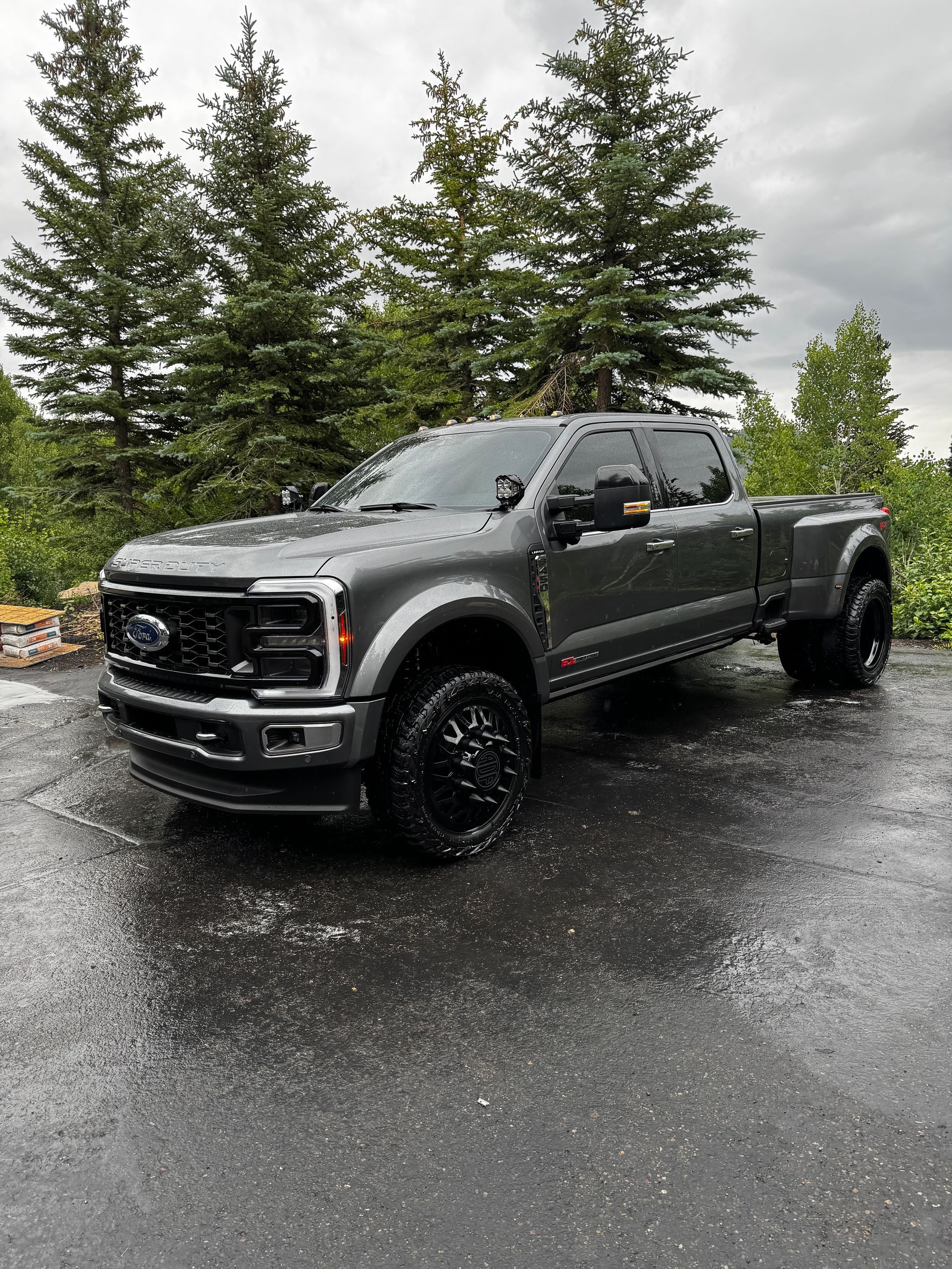 Gray lifted pickup truck parked on a wet road with evergreen trees in the background