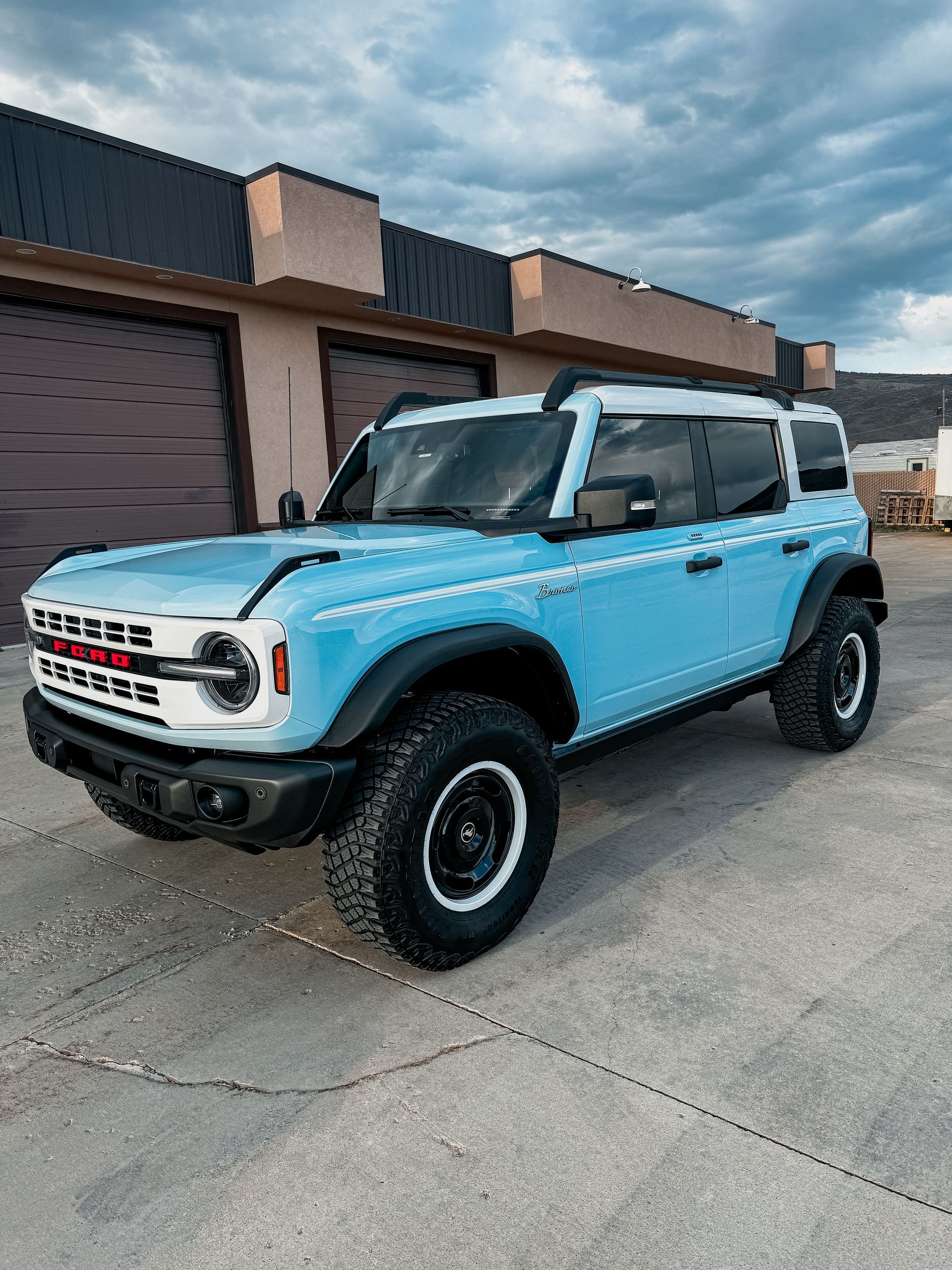 Light blue Ford Bronco SUV parked outside a building with garage doors.