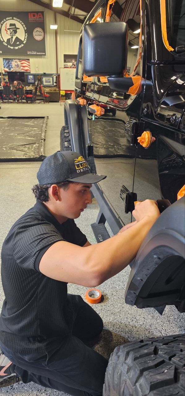 Mechanic working on a black off-road vehicle in a garage, crouched by the front wheel.