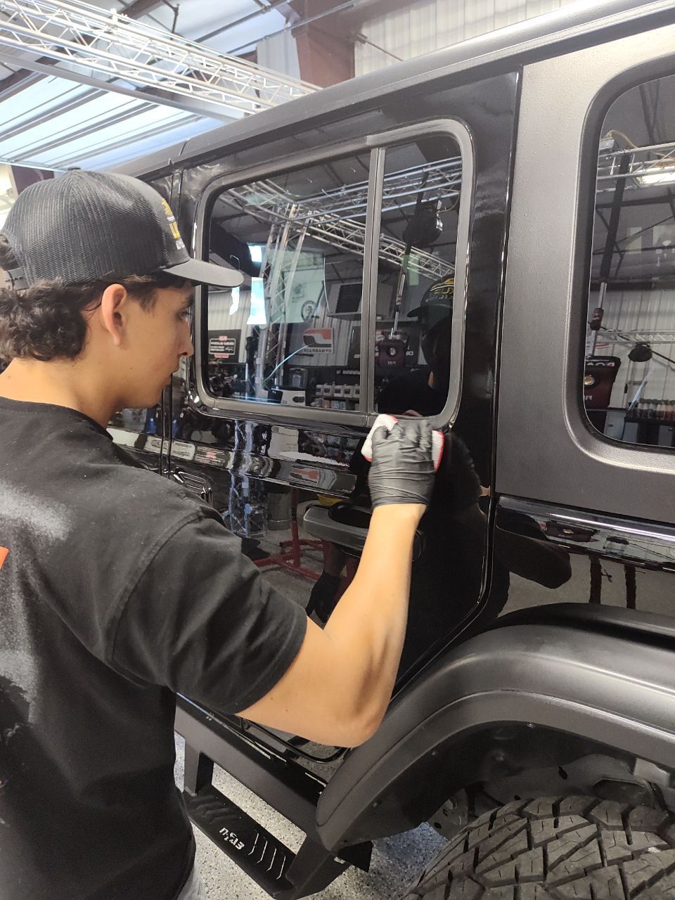 Mechanic using a power tool on a gray Jeep in an auto shop