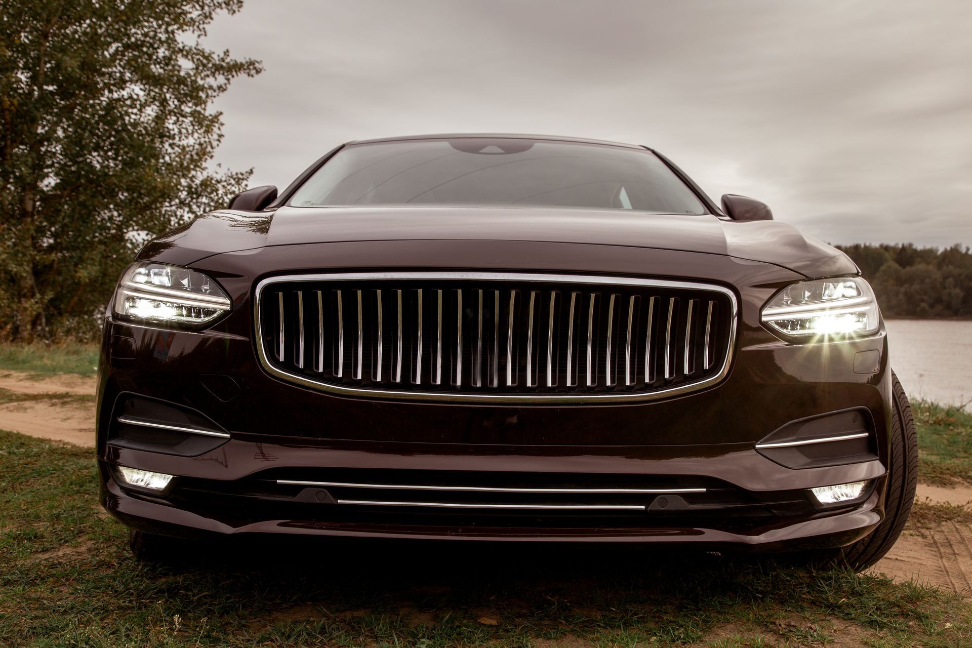 Front view of a dark luxury sedan on grass, with headlights on and a chrome grille.
