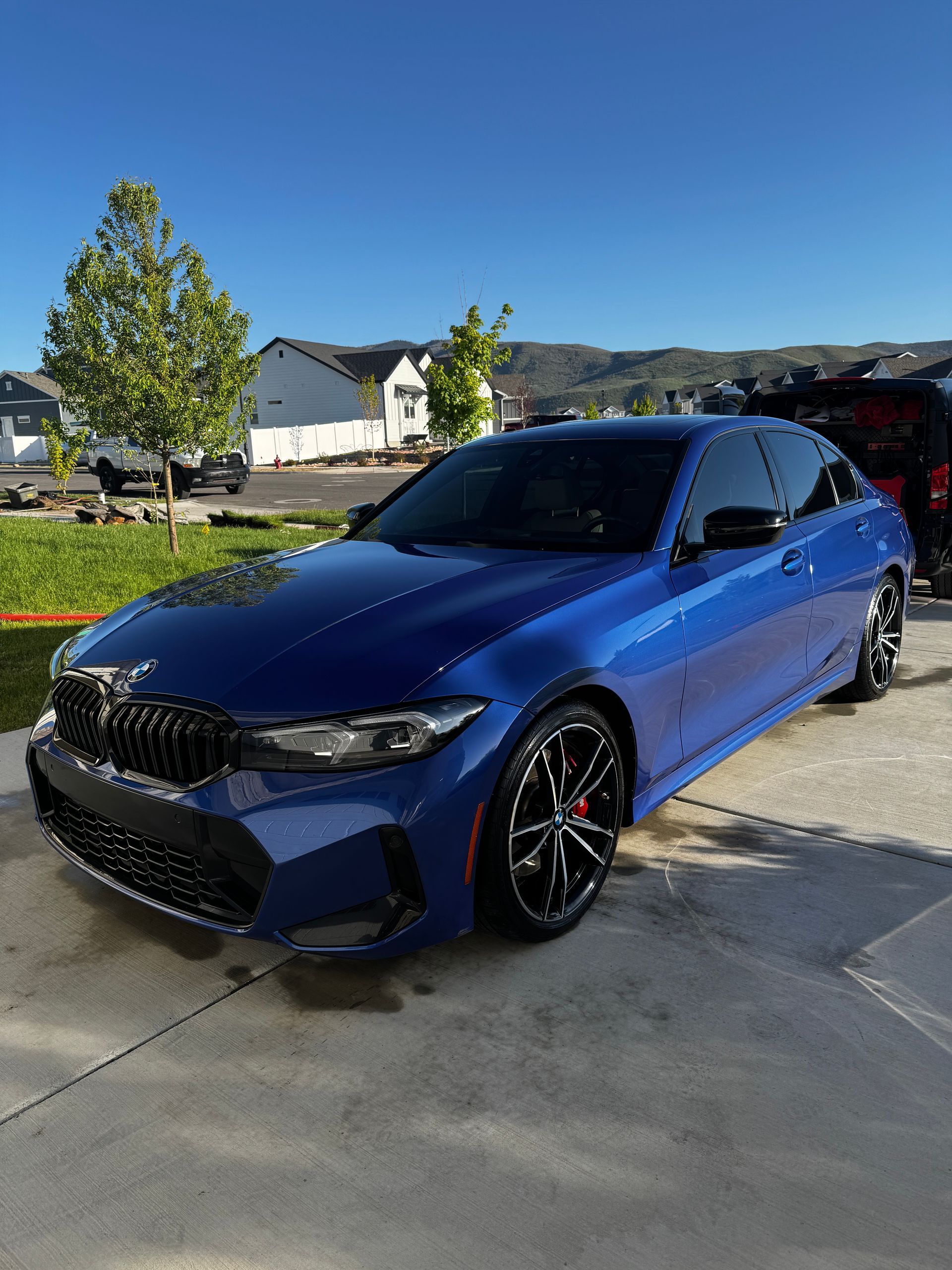 Blue BMW sedan parked in a driveway on a sunny day with houses and trees in the background