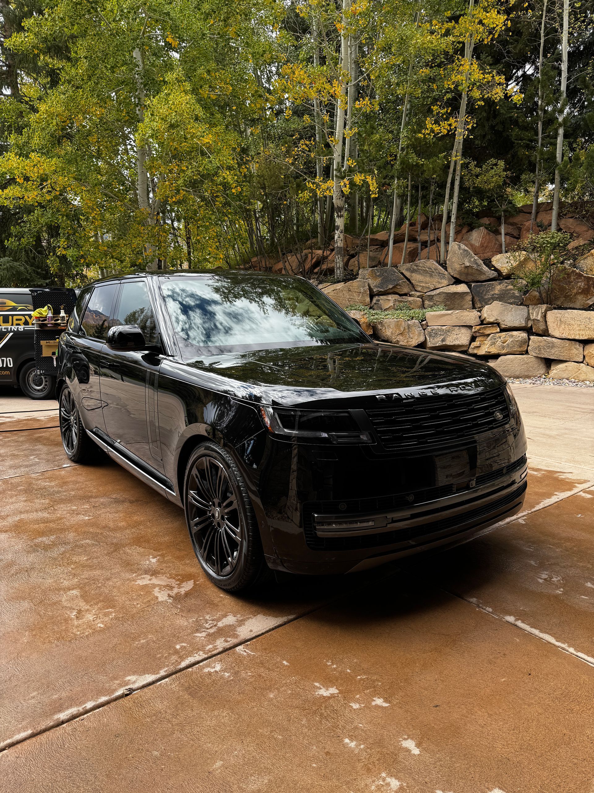 Black SUV parked on a wet driveway beside stacked stone and trees after rain