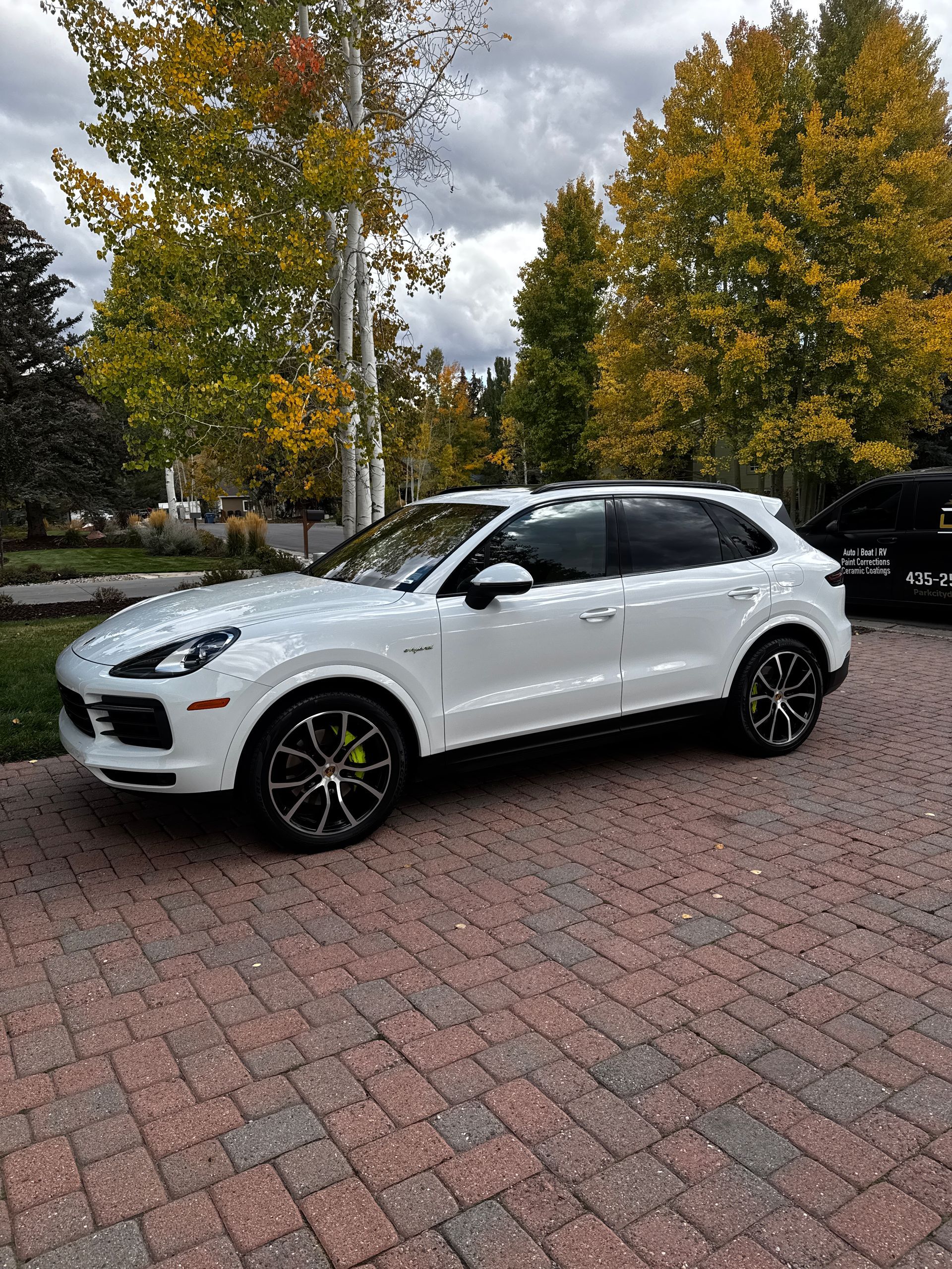 White SUV parked on a brick driveway with autumn trees in the background