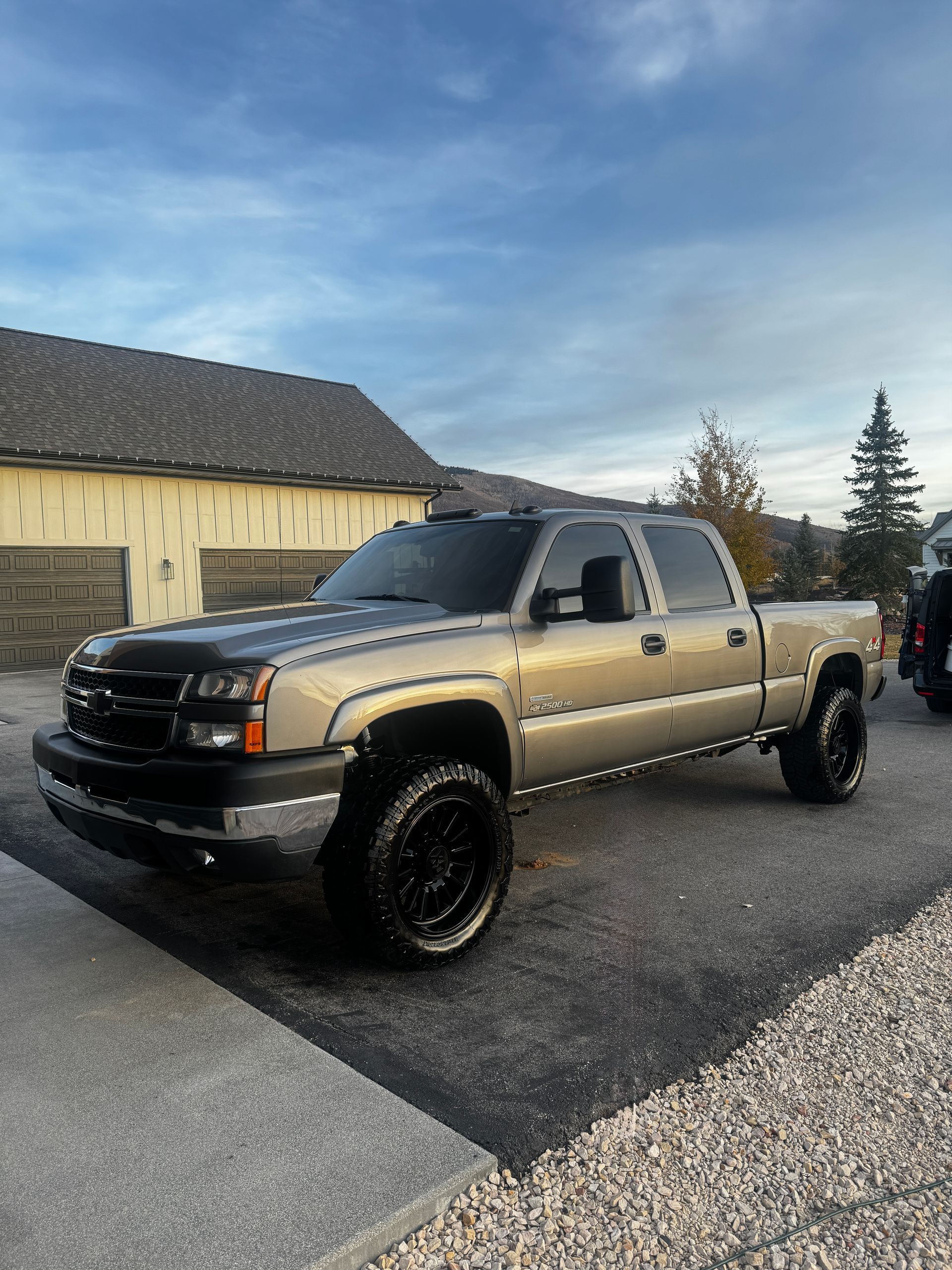Black lifted pickup truck parked in a driveway beside a house under a cloudy sky