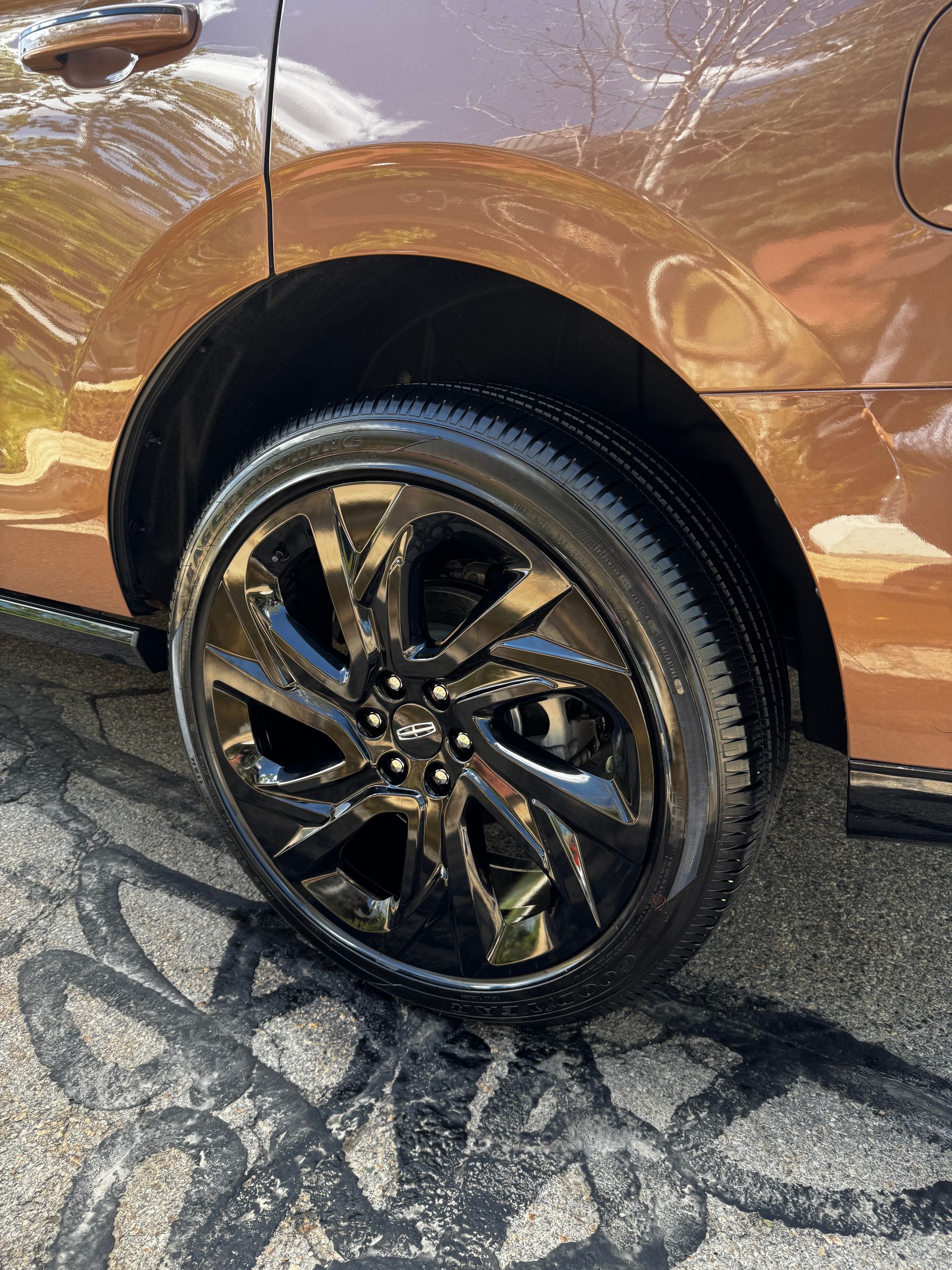 Close-up of a bronze car’s black wheel and wet tire on pavement.