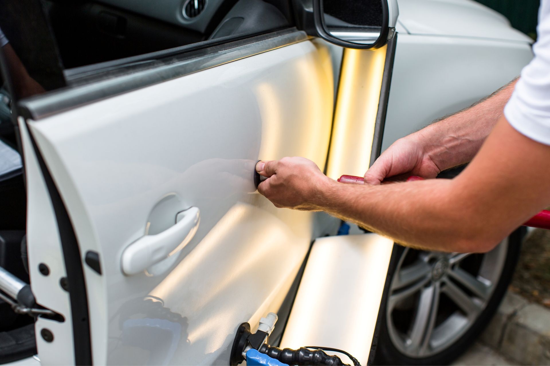 Person repairing a white car door with a tool near the window frame