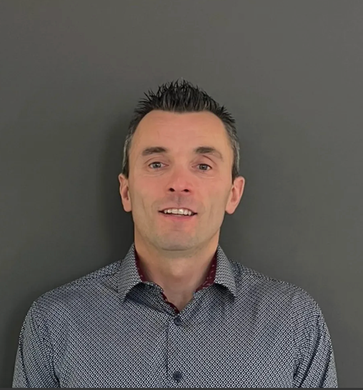 Portrait of a man in a patterned shirt standing against a plain gray background