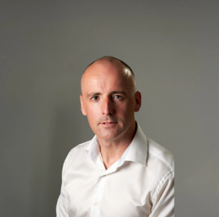 Man in a white shirt posing against a plain gray background
