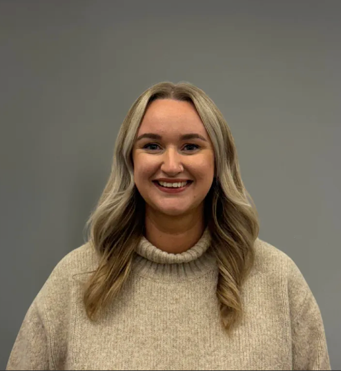 Smiling woman in a beige sweater against a plain gray background