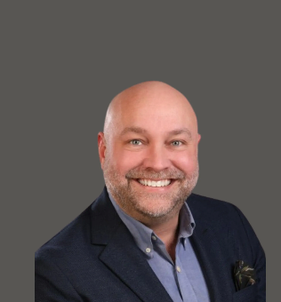 Smiling bald man in a navy blazer against a gray background