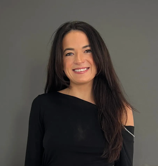 Smiling woman with long dark hair in a black top against a gray background