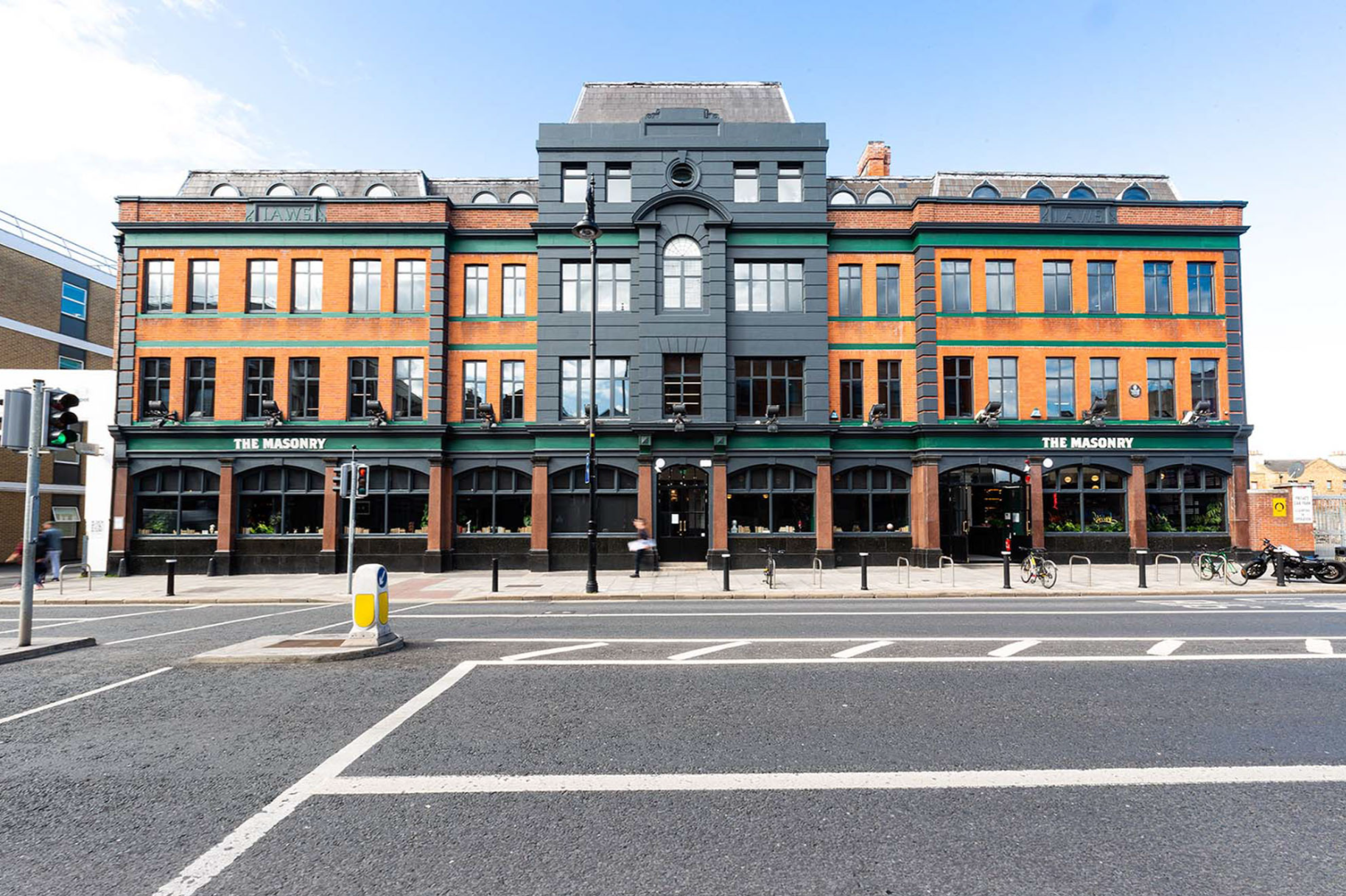 Street view of a brick-and-green historic building with storefronts and black awnings across the road