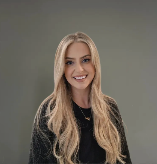 Smiling blonde woman in a black top against a plain gray background
