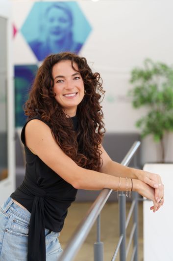 Smiling woman with long dark hair in a black top against a gray background