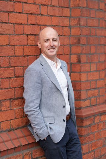 Man in a white shirt posing against a plain gray background