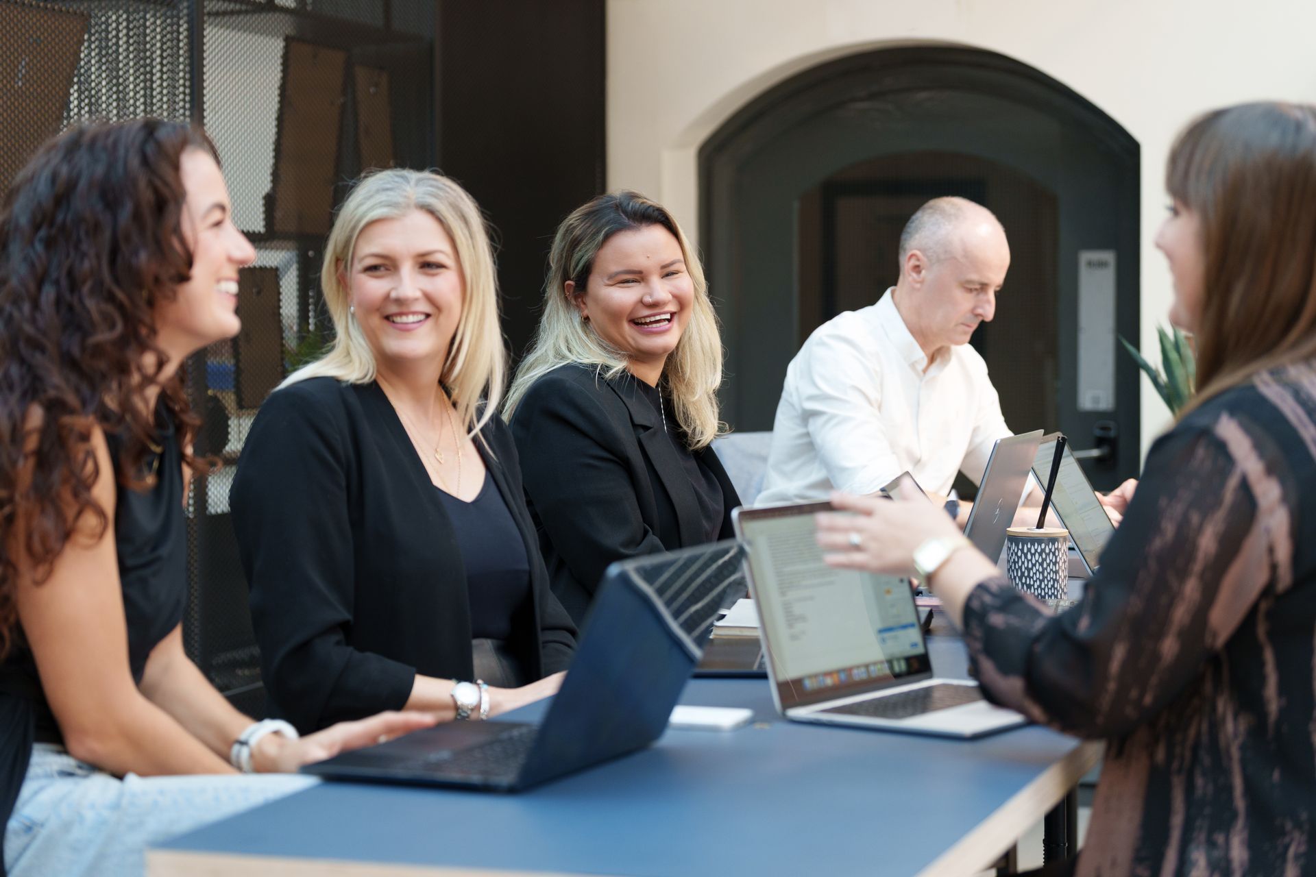 Three coworkers chatting around a laptop in a warm-lit office lounge