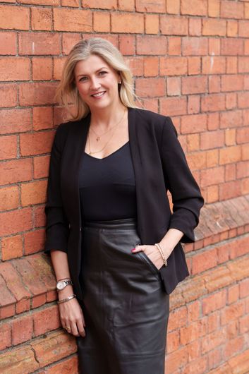 Smiling blonde woman in a black top against a plain gray background