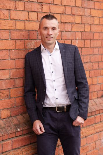 Person in a patterned shirt posing against a plain gray background.