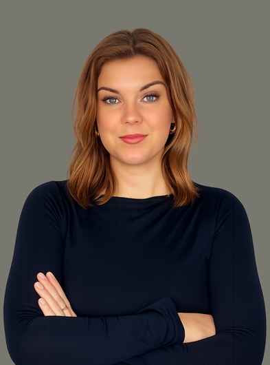 Portrait of a person with crossed arms, wearing a dark long-sleeve top against a plain gray background
