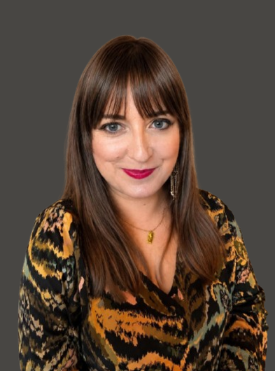 Portrait of a smiling person with long brown hair wearing a black-and-gold patterned top.