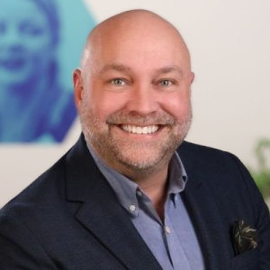 Smiling bald man in a navy blazer against a gray background