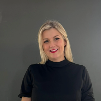 Smiling blonde woman in a black top against a plain gray background