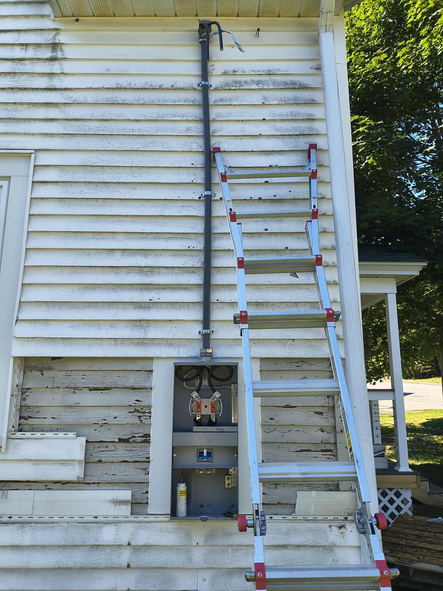 Ladder leaning against house siding beside utility meters and a pole