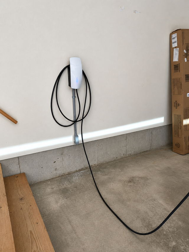Wall-mounted white EV charger with coiled black cable in a garage near the floor.