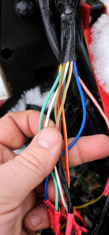 A hand holds a bundle of multicolored wires inside a black wrapped cable near a vehicle panel.