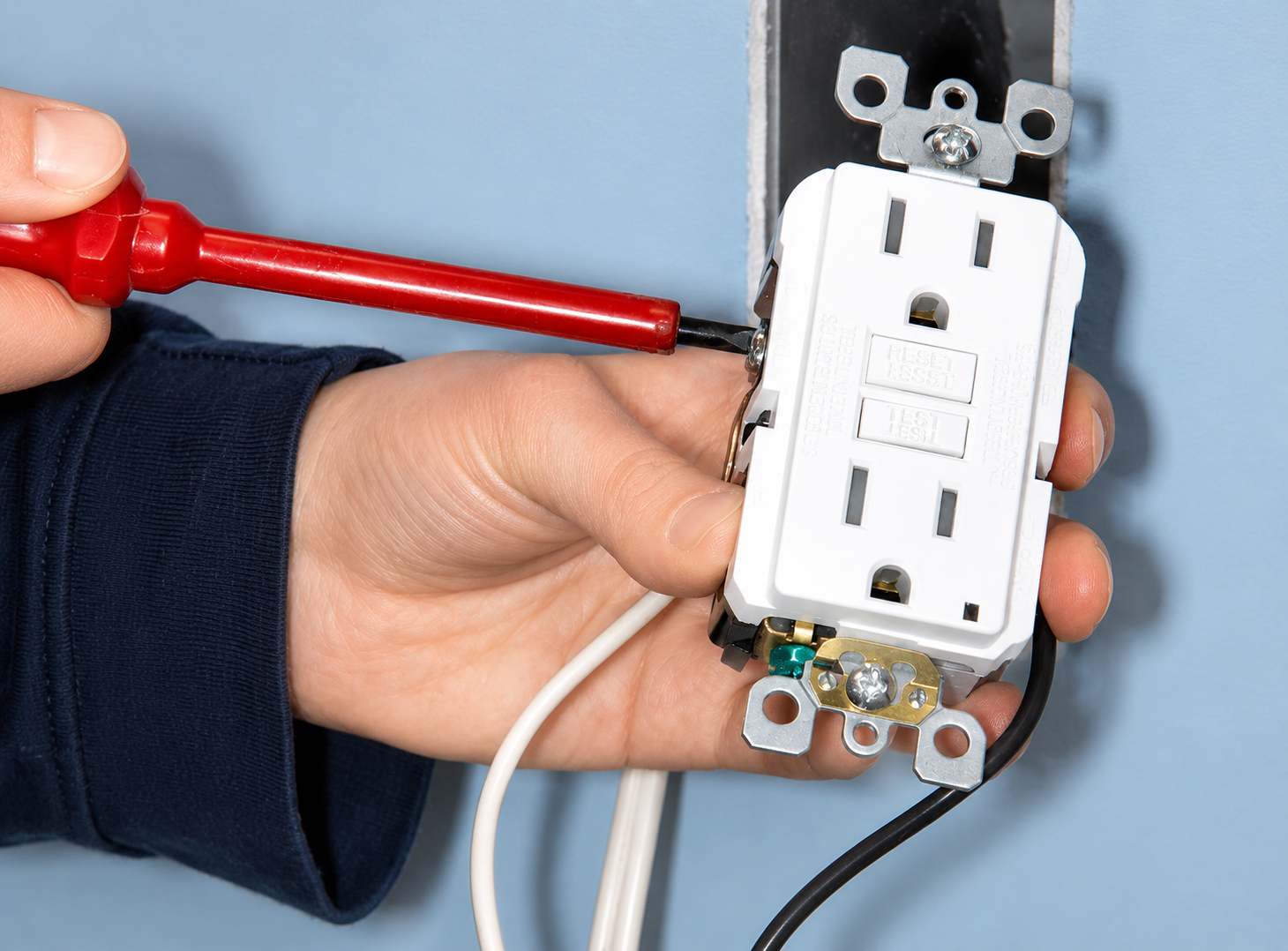 Hand holding a white electrical outlet being tightened with a red screwdriver