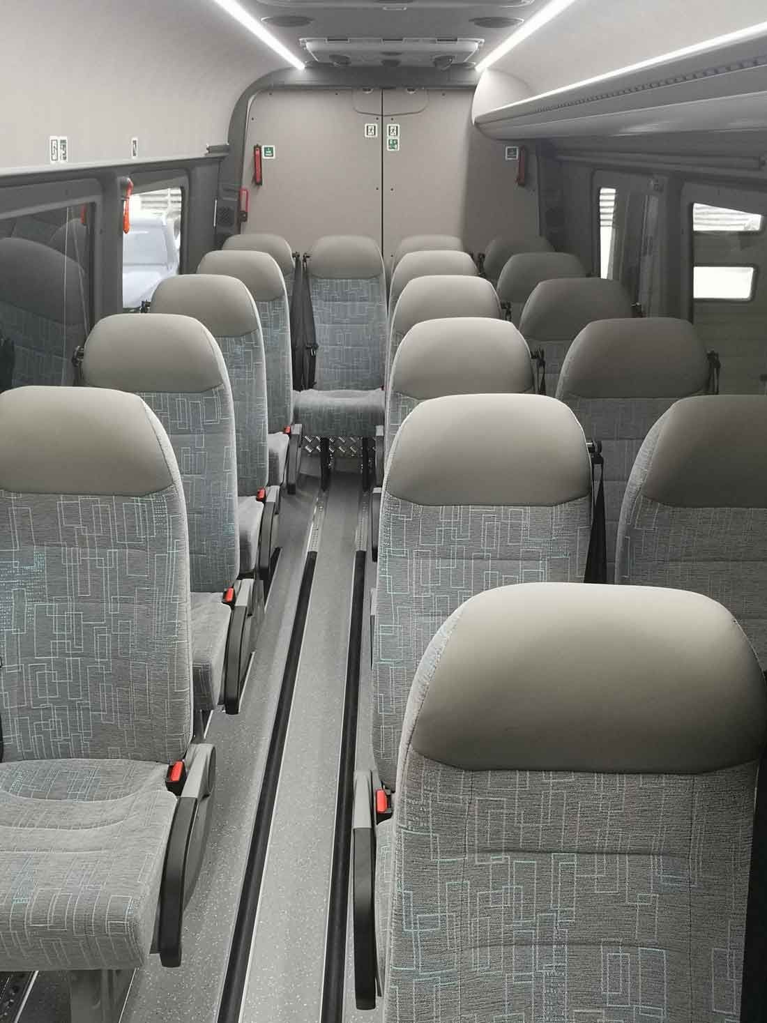 Interiør i en bus med rækker af grå polstrede sæder og en midtergang.