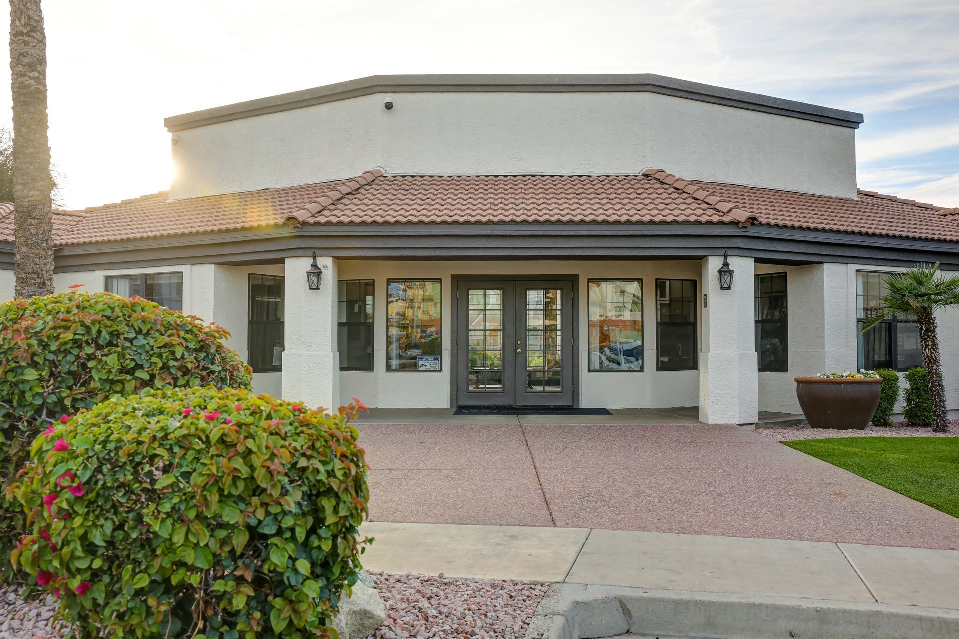 Front view of a stucco building with a red-tiled roof, double doors, and landscaped entrance
