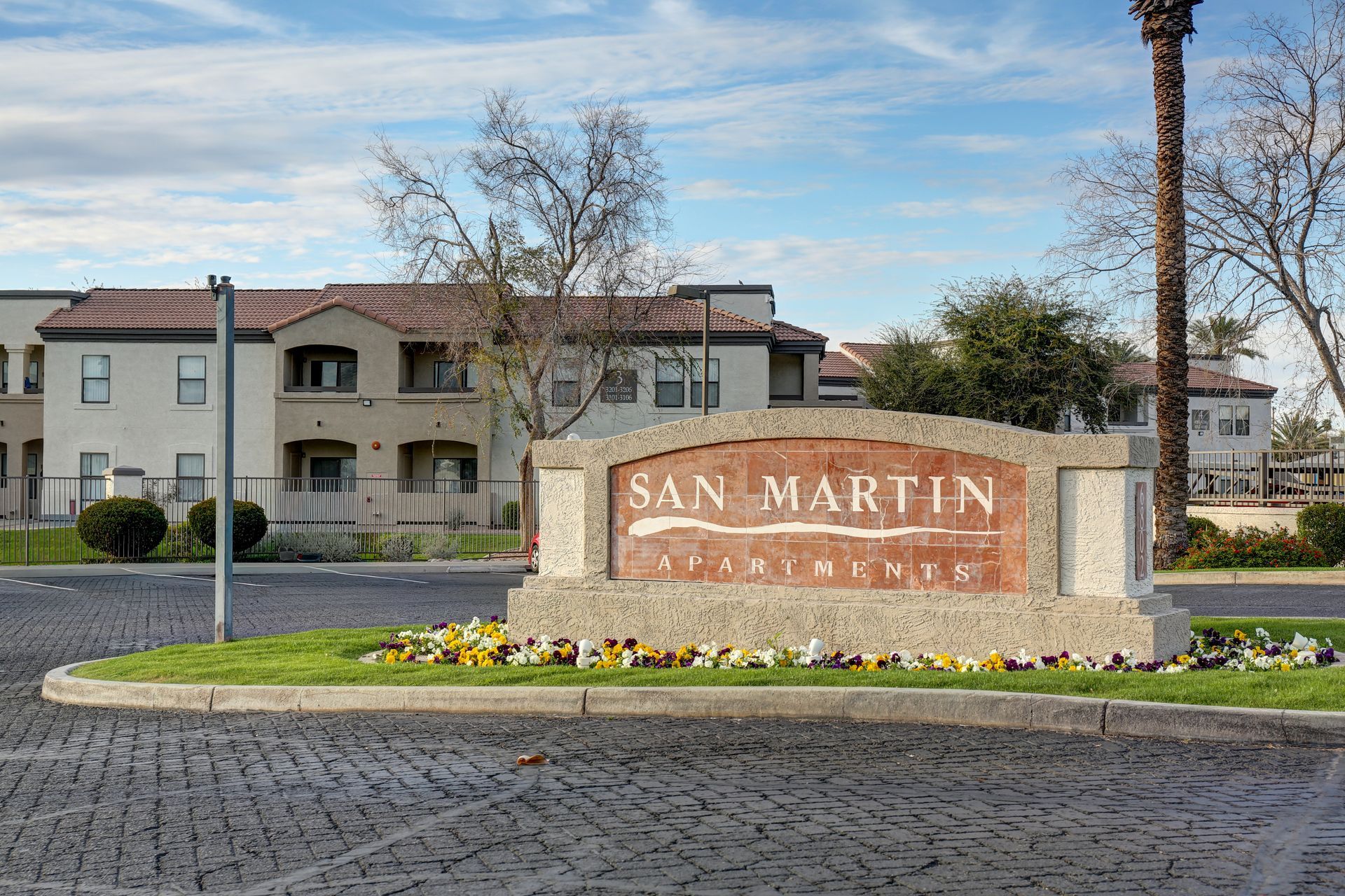 San Martin apartment entrance sign with stone monument, flower bed, and buildings in the background