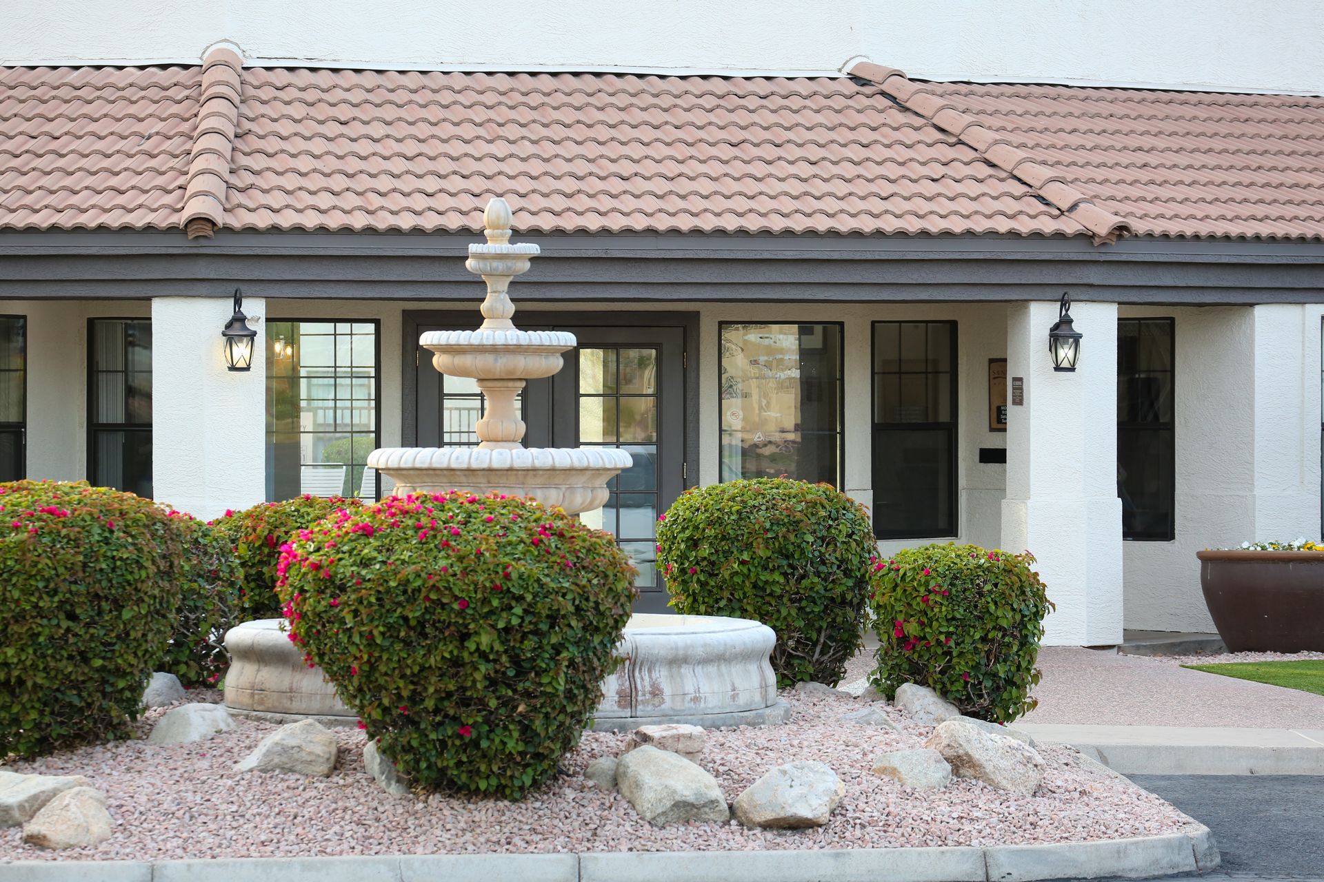 Front of a suburban house with a stone fountain, trimmed shrubs, and a tiled roof