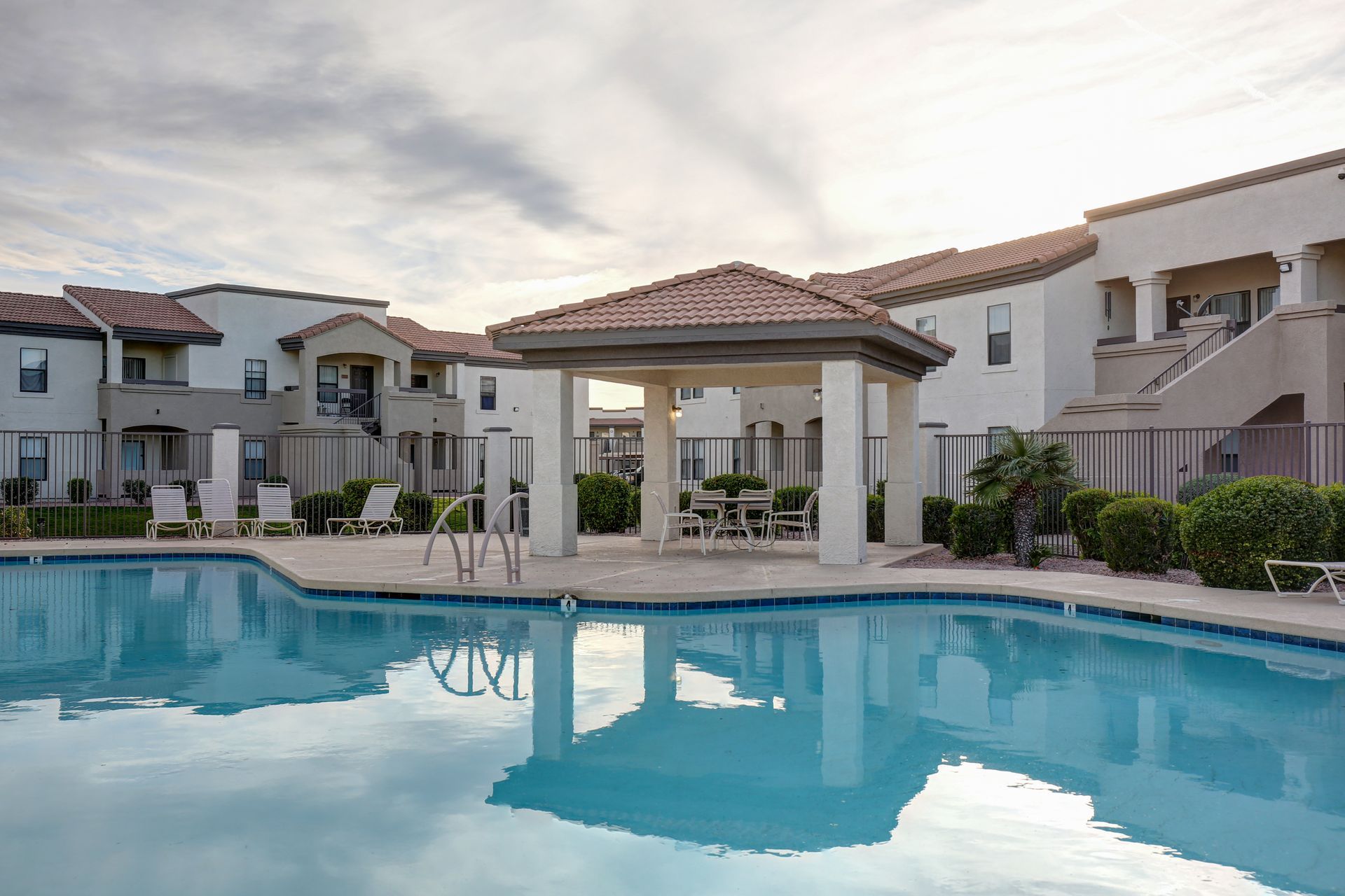 Resort-style swimming pool with a gazebo and beige apartment buildings under a clear sky