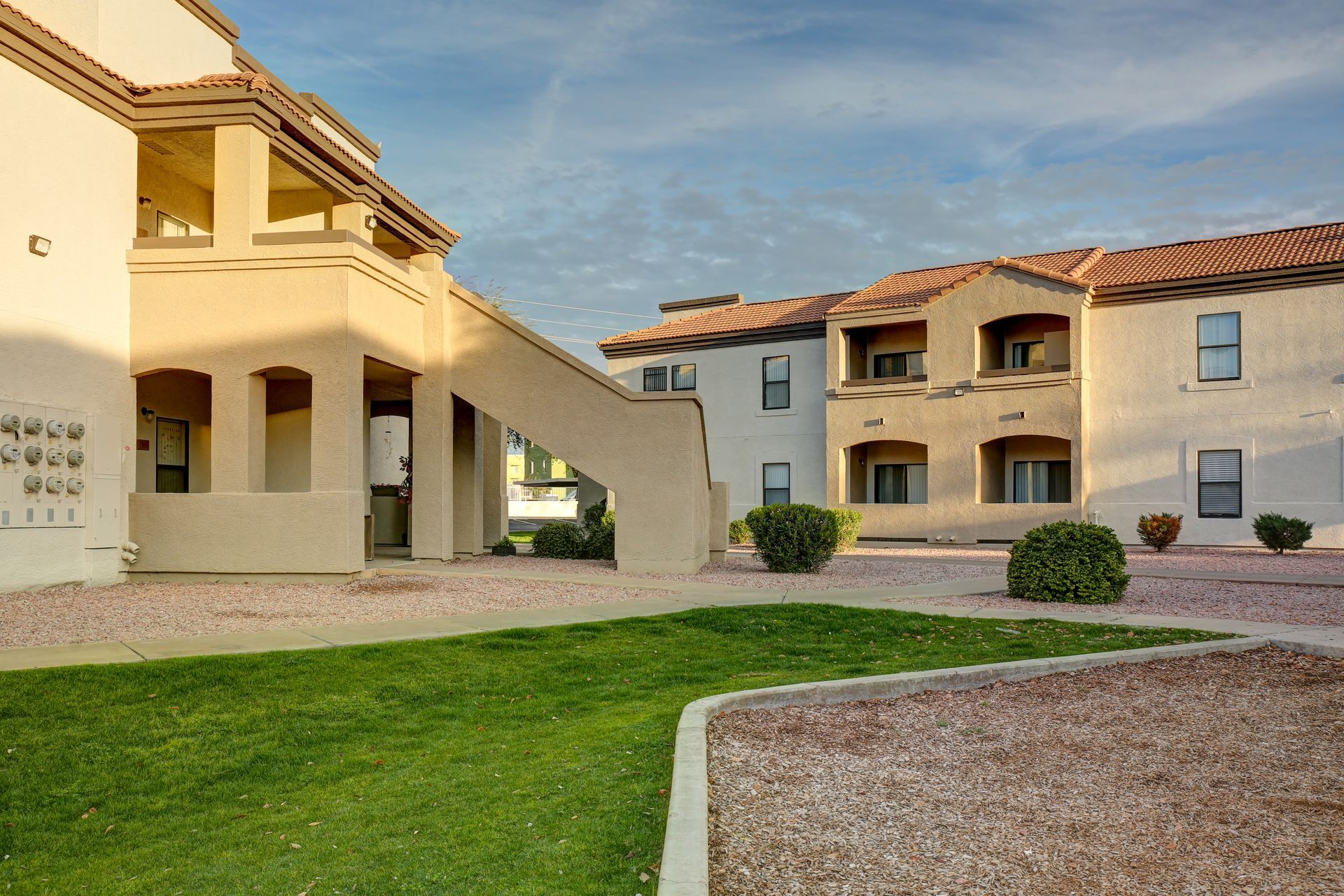 Apartment courtyard with beige buildings, green lawn, and gravel paths under warm sunlight