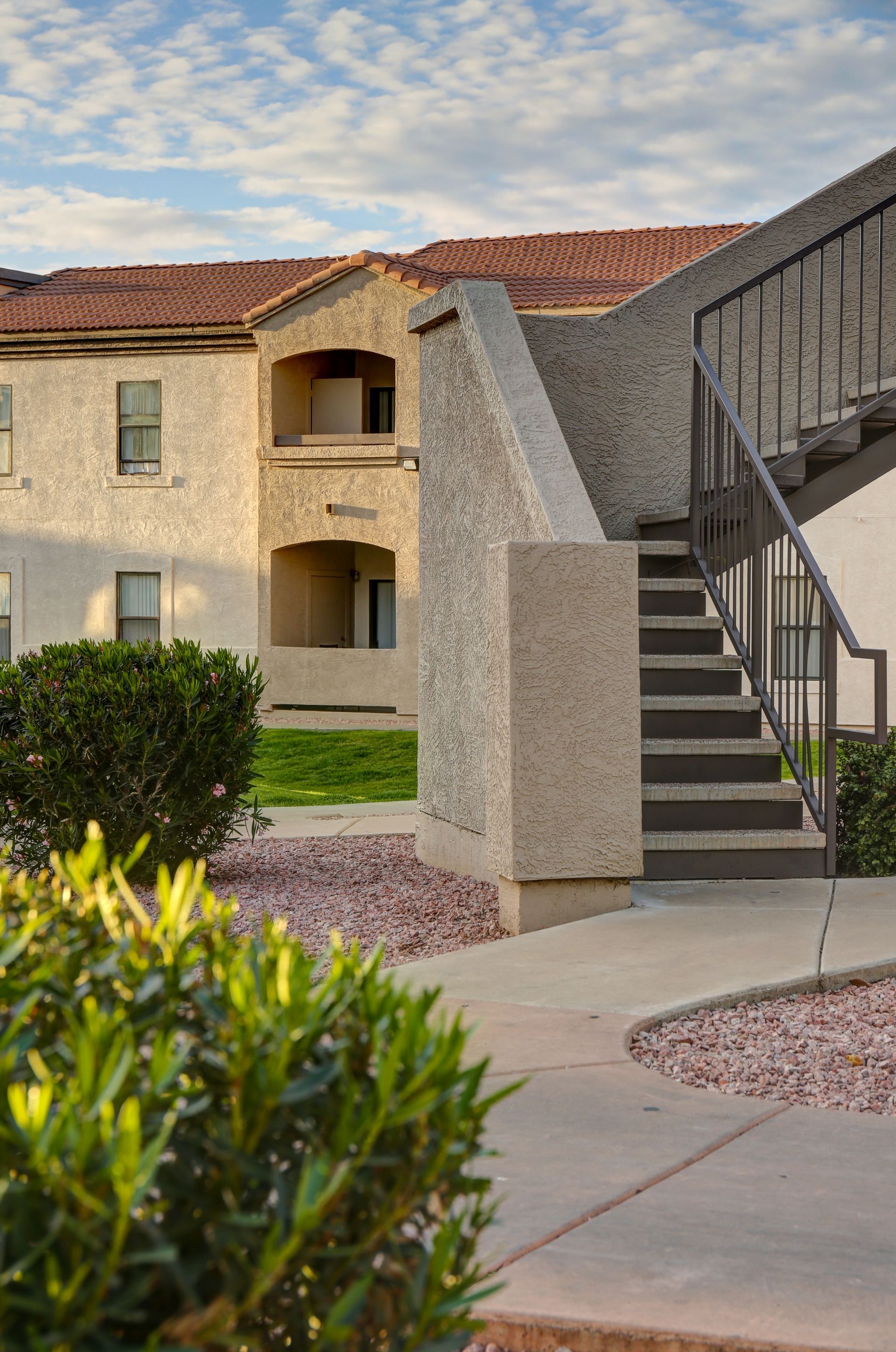 Apartment courtyard with tan buildings, red tile roofs, stairs, and landscaped shrubs