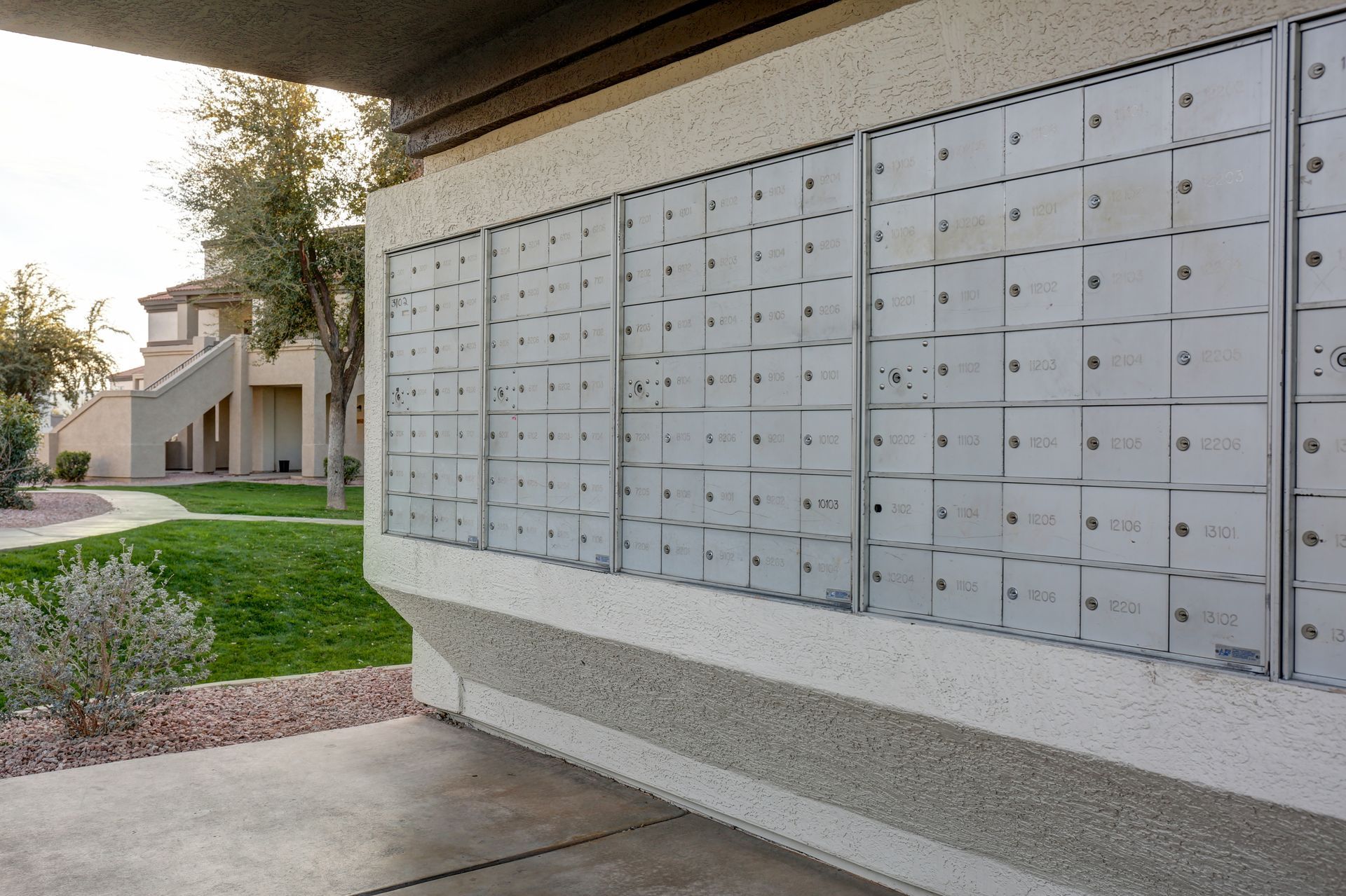 Rows of apartment mailboxes along a covered outdoor walkway beside a grassy courtyard