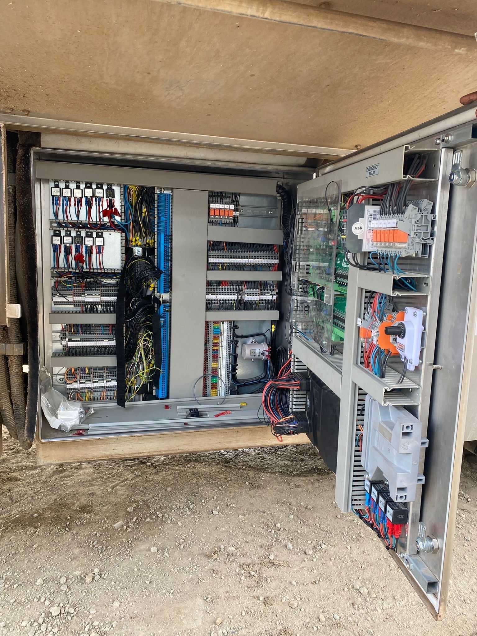 Open electrical control panel with various wiring, circuit breakers, and components in an outdoor setting.