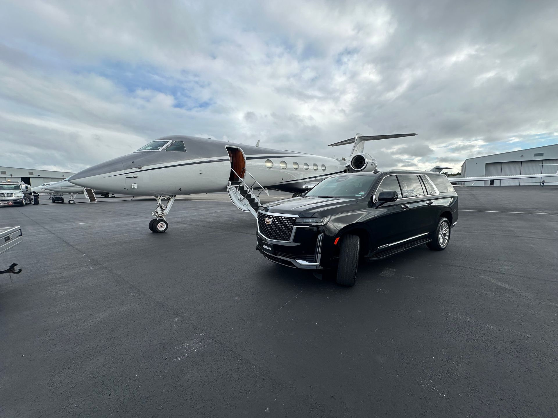 Black Cadillac Escalade ESV waiting planeside next to a private jet at a Miami FBO — 515 MIAMI VIP car service