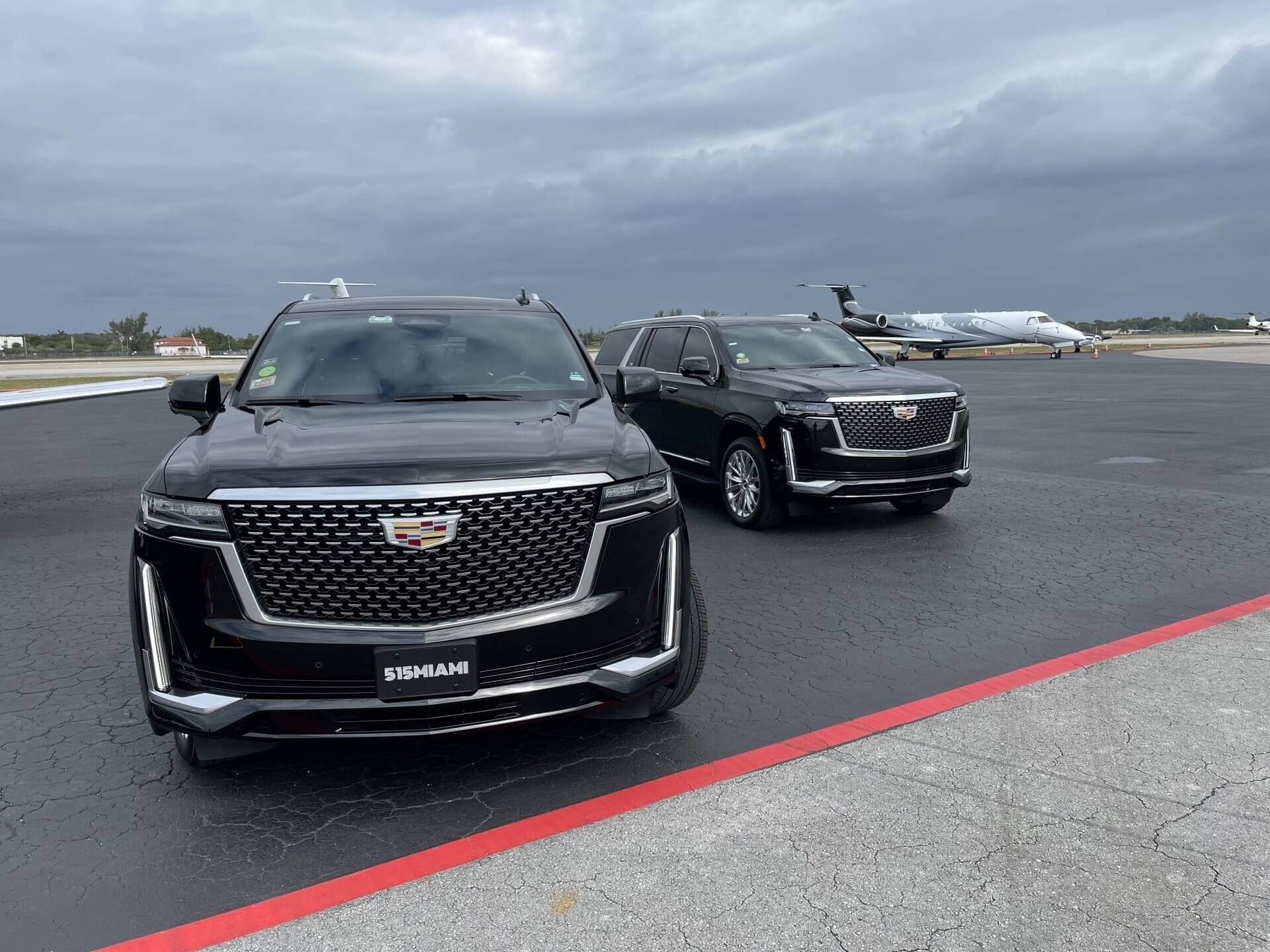 Two black Cadillac Escalade SUVs on the tarmac for a VIP airport transfer in Miami