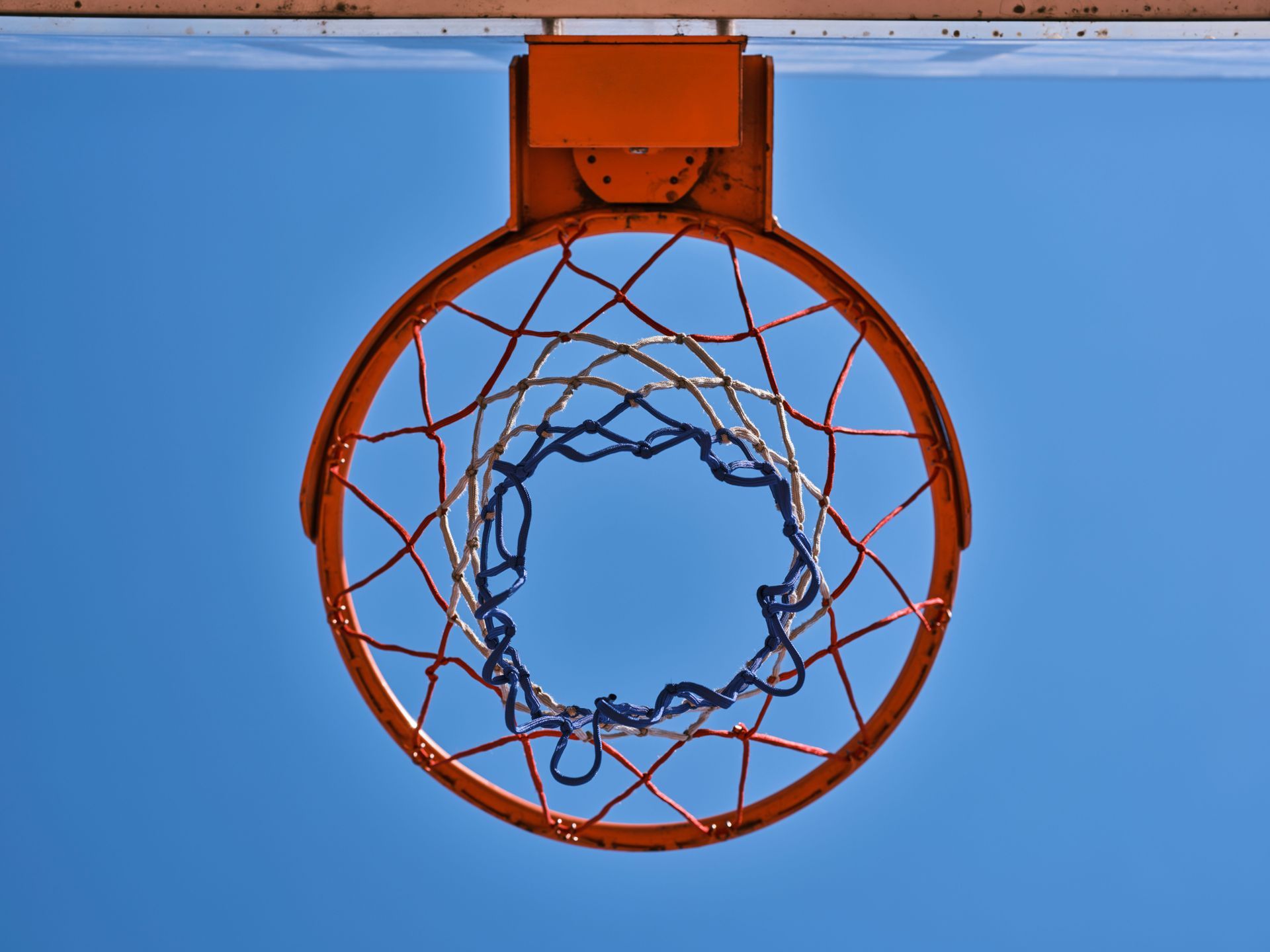 Basketball rim and red white and blue net seen from directly underneath against a blue sky
