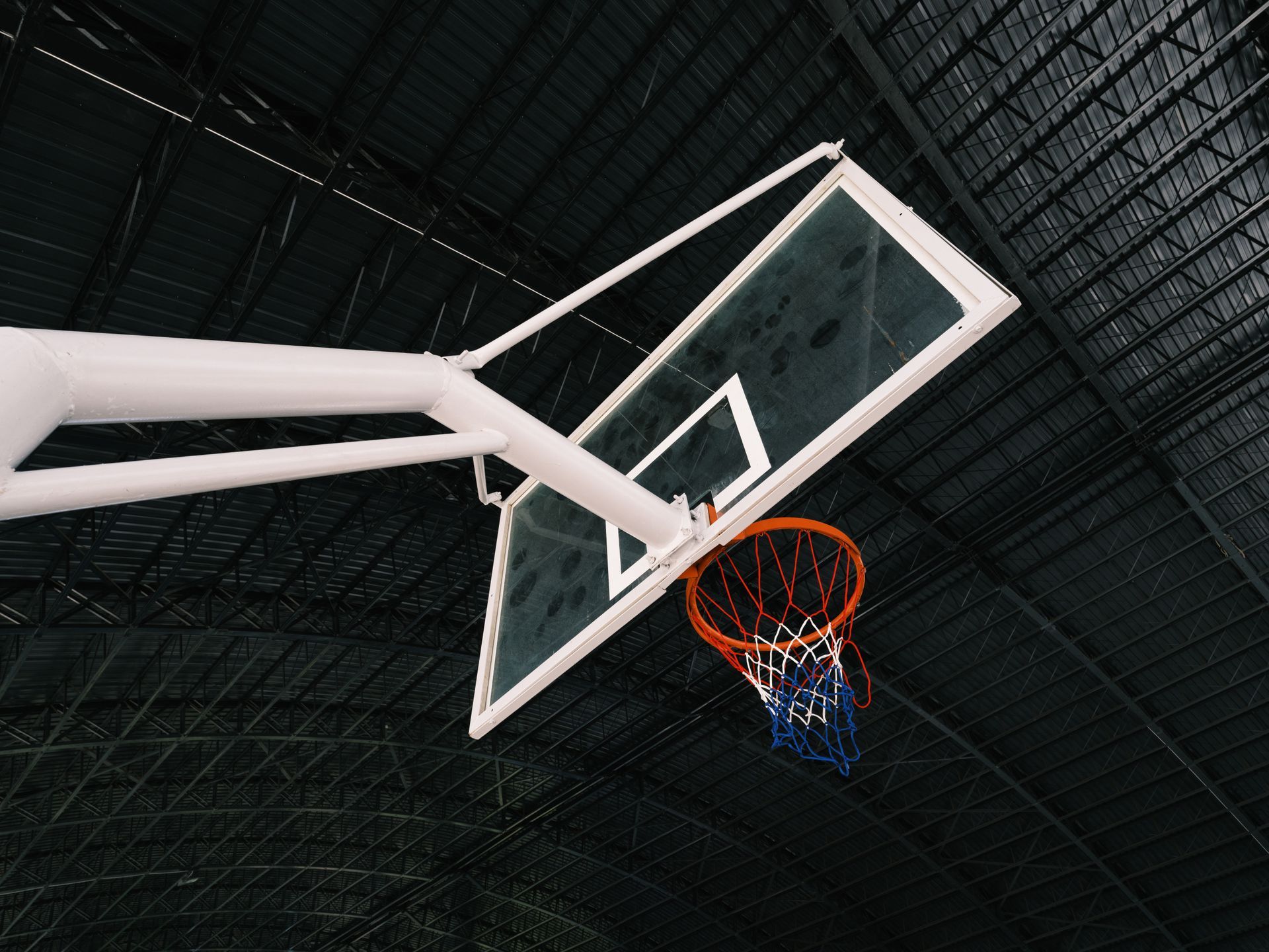 Basketball hoop and glass backboard below the dark roof of an arena