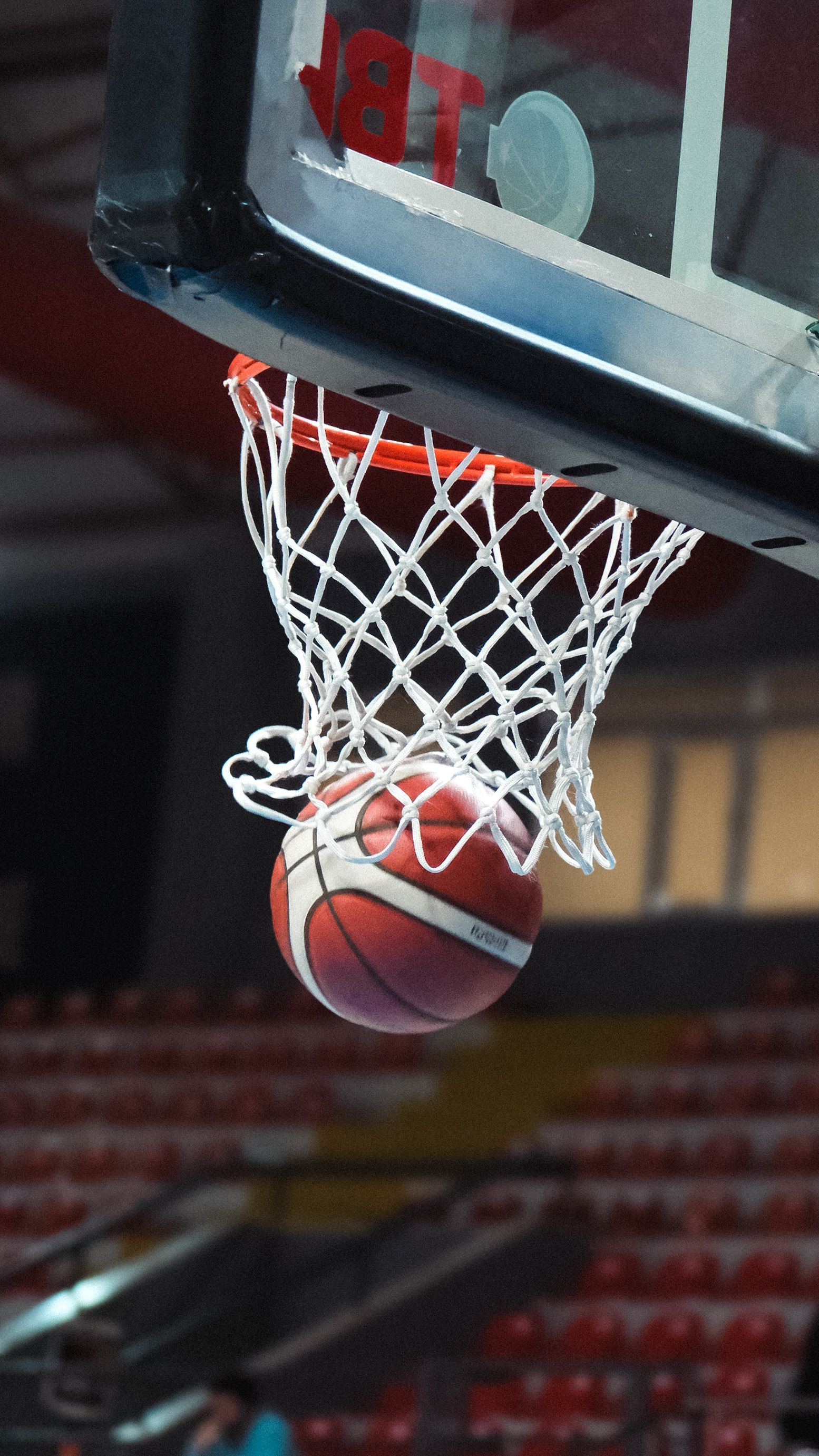 A basketball dropping through the net of an indoor basketball hoop