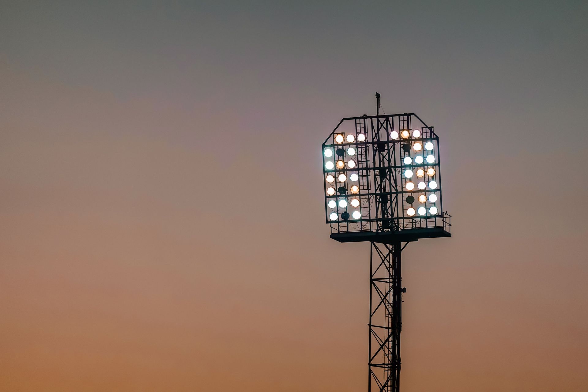 Stadium floodlight tower lit against a warm amber evening sky