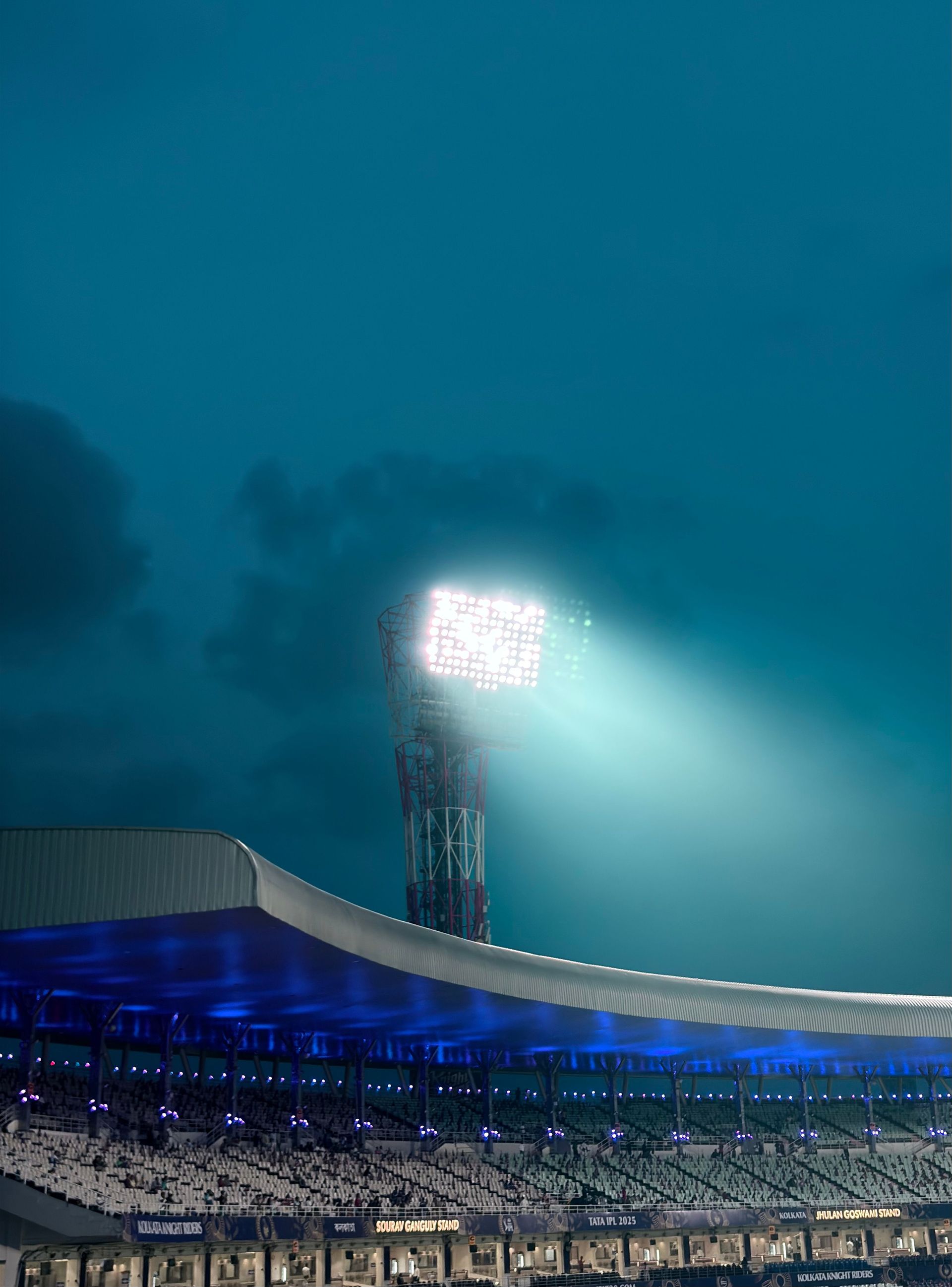 Stadium floodlight beam cutting through night fog above a stadium roof