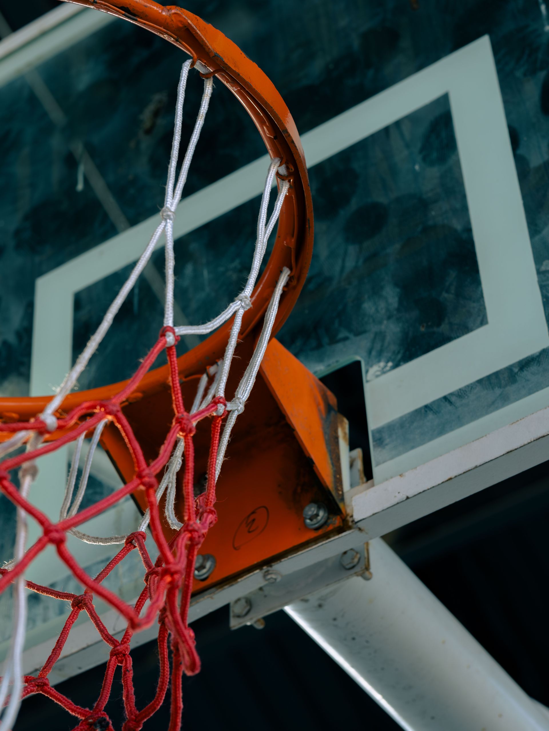 Weathered basketball rim and net on a glass backboard in a sports hall