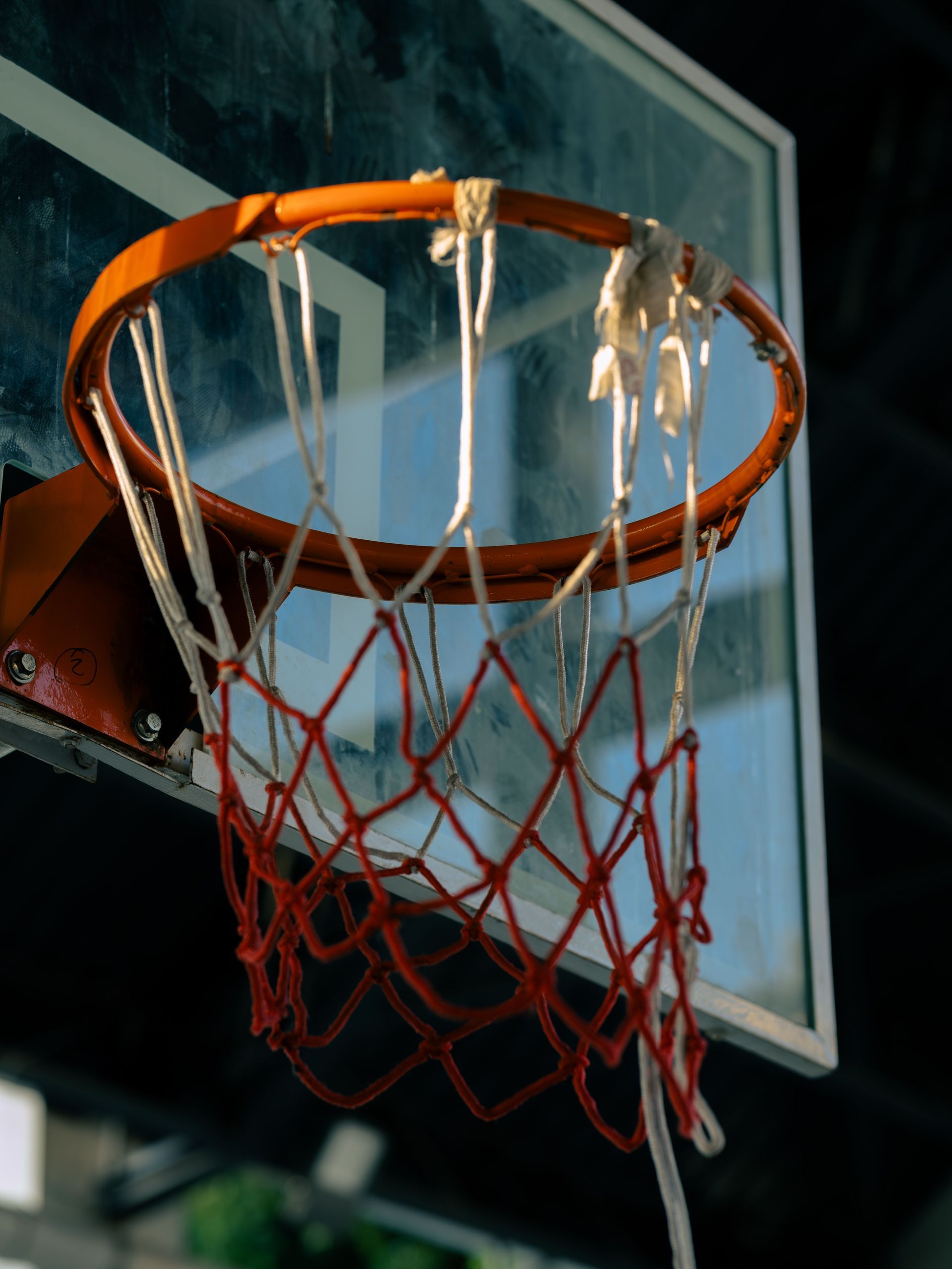 Worn orange basketball rim and red net hanging below a glass backboard