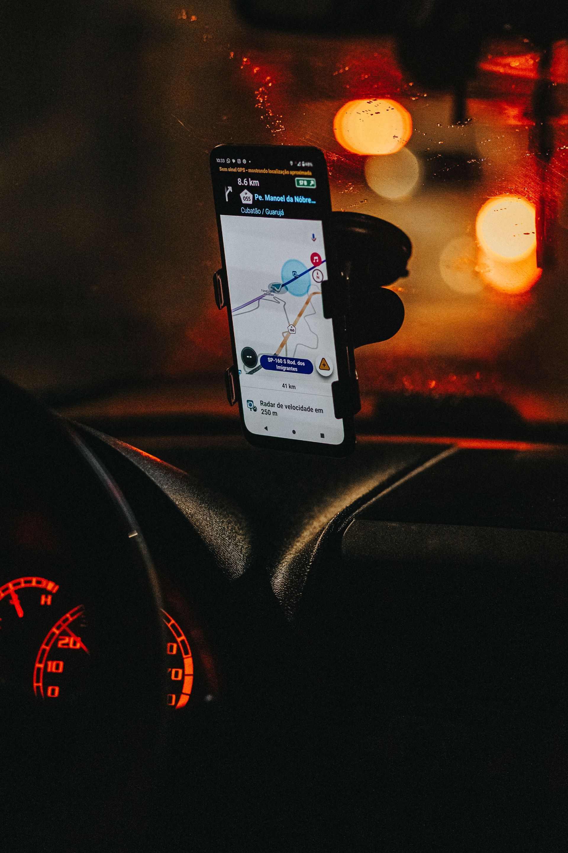 A smartphone mounted on a car dashboard showing a navigation map on a city street at night